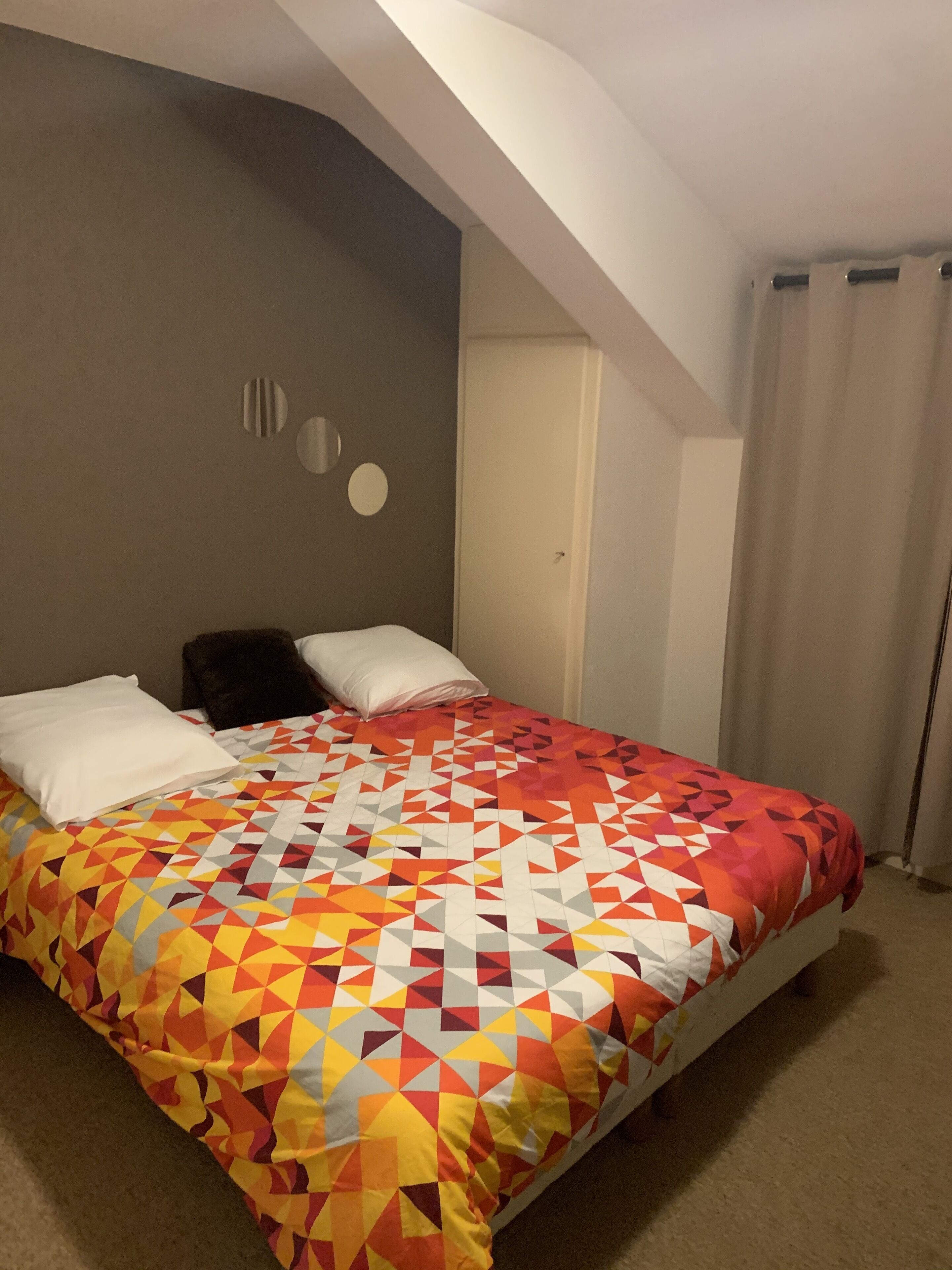A bedroom with a bed, a door, and a window with curtains.