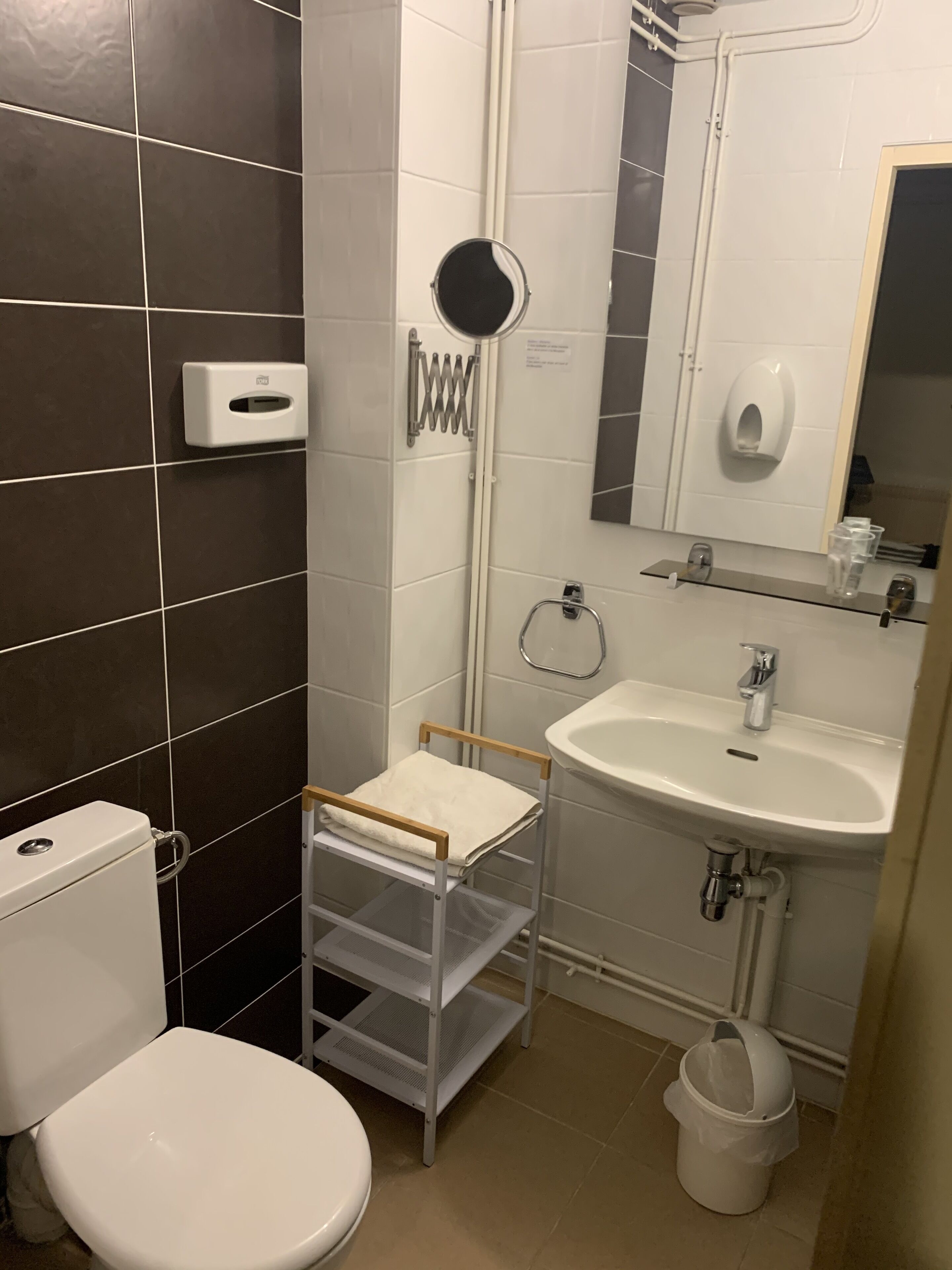 A compact bathroom with a toilet, sink, and a small shelf unit.