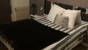 A bed with striped bedding, a black throw blanket, and several pillows. - Hotel bon accueil (Oyonnax)
