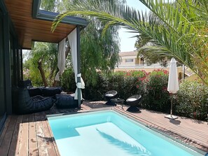 A pool area with a wooden deck, black cushioned seating, and a canopy structure. - VILLA LARES at 150m from the beach of Cala Mendia (porto cristo novo)