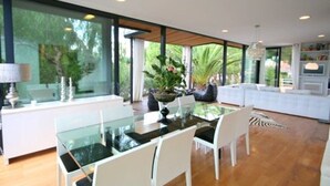 Un'area pranzo moderna con un tavolo in vetro, sedie bianche e vista sul verde circostante.