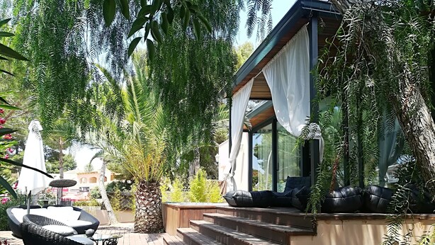 Un terrazza in legno con posti a sedere all'aperto, una scala che conduce a una zona riparata e una vegetazione rigogliosa.