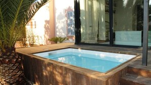 Una vasca idromassaggio in legno rettangolare con fondo in vetro, circondata da un pontile in legno e palme.