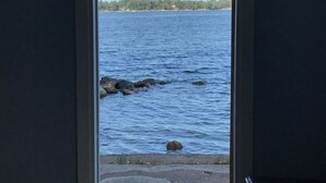 A door leading to a view of a calm body of water with rocks and a distant shoreline.
