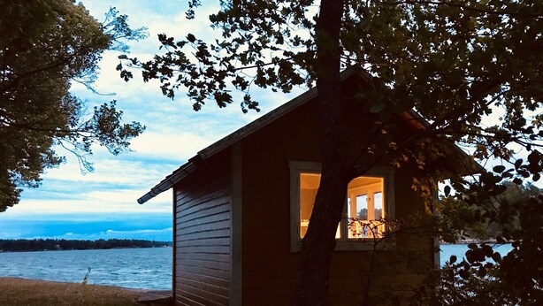 A small wooden cabin with a window, situated by a body of water.