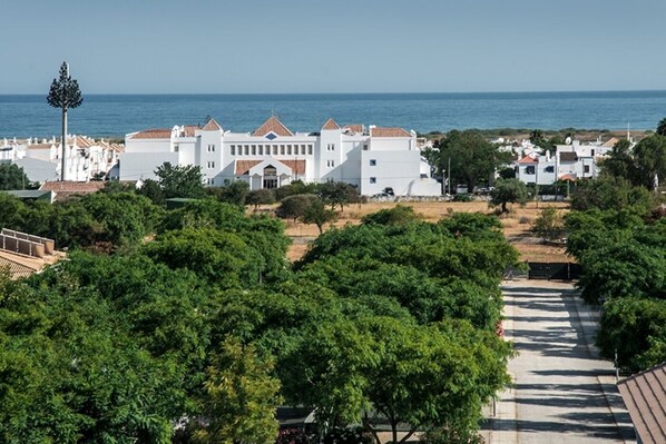 A coastal hotel with a central building surrounded by lush greenery and a clear view of the sea.