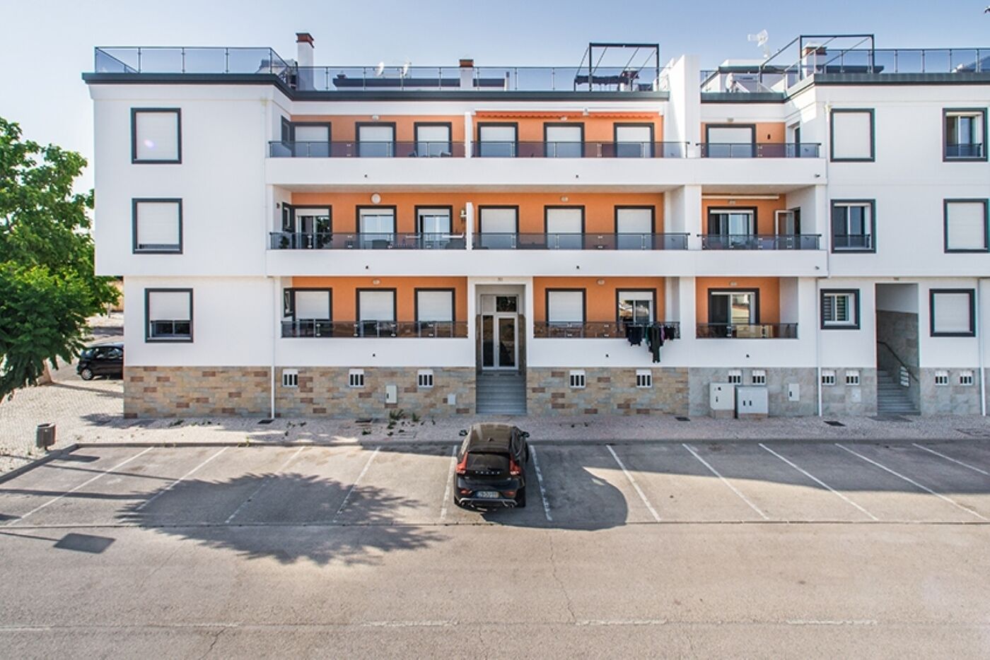Un hotel de varios pisos con un diseño moderno, con balcones en cada planta, un estacionamiento al frente y una vista despejada de la entrada.