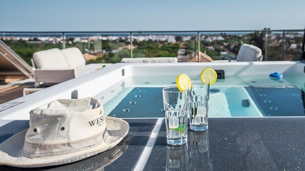 A sunlit outdoor seating area with a pool table, two glasses of water with lemon slices, and a hat on a table. - Luxurious Apartment with Private Terrace & Jacuzzi (Tavira)