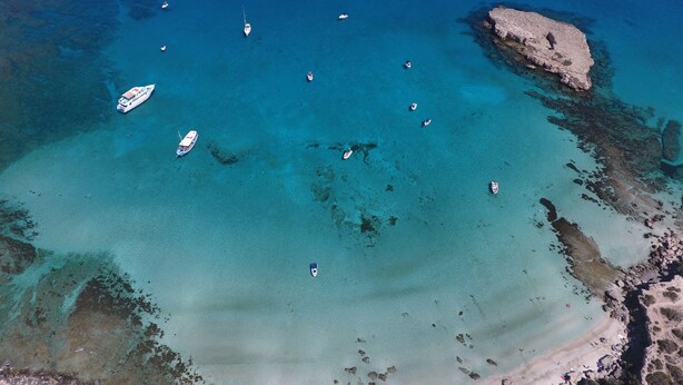 An aerial view of a coastal area with clear turquoise waters, several boats, and rocky formations.
