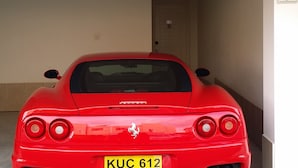 A red sports car parked in a covered garage with a yellow license plate.