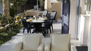 A patio area with wicker furniture, a glass table with a floral centerpiece, and a dining table with chairs and an umbrella.