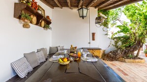 A dining area with a long table set for breakfast, surrounded by cushioned seating, and a rustic wooden ceiling. - Monte da Luz - Casa da Mó (Luz)