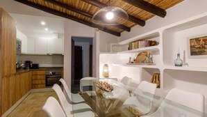 A modern kitchen with white cabinets, a built-in oven, and a dining area with a glass table and white chairs. - Monte da Luz - Casa da Mó (Luz)