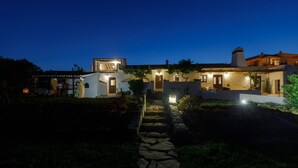 A well-lit villa with a stone pathway leading to the entrance, surrounded by lush greenery. - Monte da Luz - Casa da Mó (Luz)