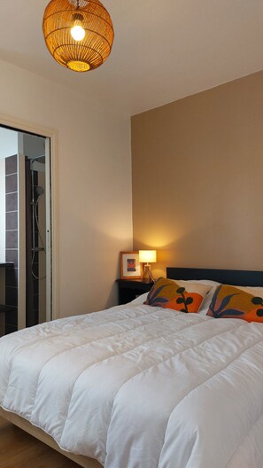 A hotel room with a bed, a nightstand with a lamp, a framed picture, and a shower area. - Vacation Home on the Pink Granite Coast (Trébeurden)