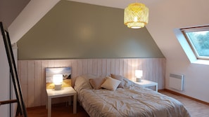 A bedroom with a sloped ceiling, a bed with pillows, a bedside table with a lamp, a painting on the wall, and a window.