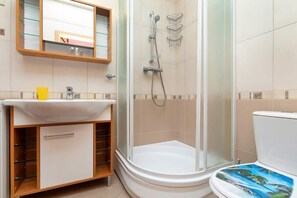 Un baño con ducha acristalada, lavamanos blanco y retrete con motivos tropicales.