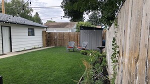 A backyard with a well-maintained lawn, two Adirondack chairs, a wooden fence, and a shed. - Walk to Hospital - Medical Workers Suite (Lethbridge)