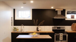 A modern kitchen with a black backsplash, stainless steel appliances, a wooden countertop, and a window above the sink. - Walk to Hospital - Medical Workers Suite (Lethbridge)