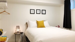 A neatly arranged bedroom with a bed, bedside table, lamp, and wall art. - Walk to Hospital - Medical Workers Suite (Lethbridge)