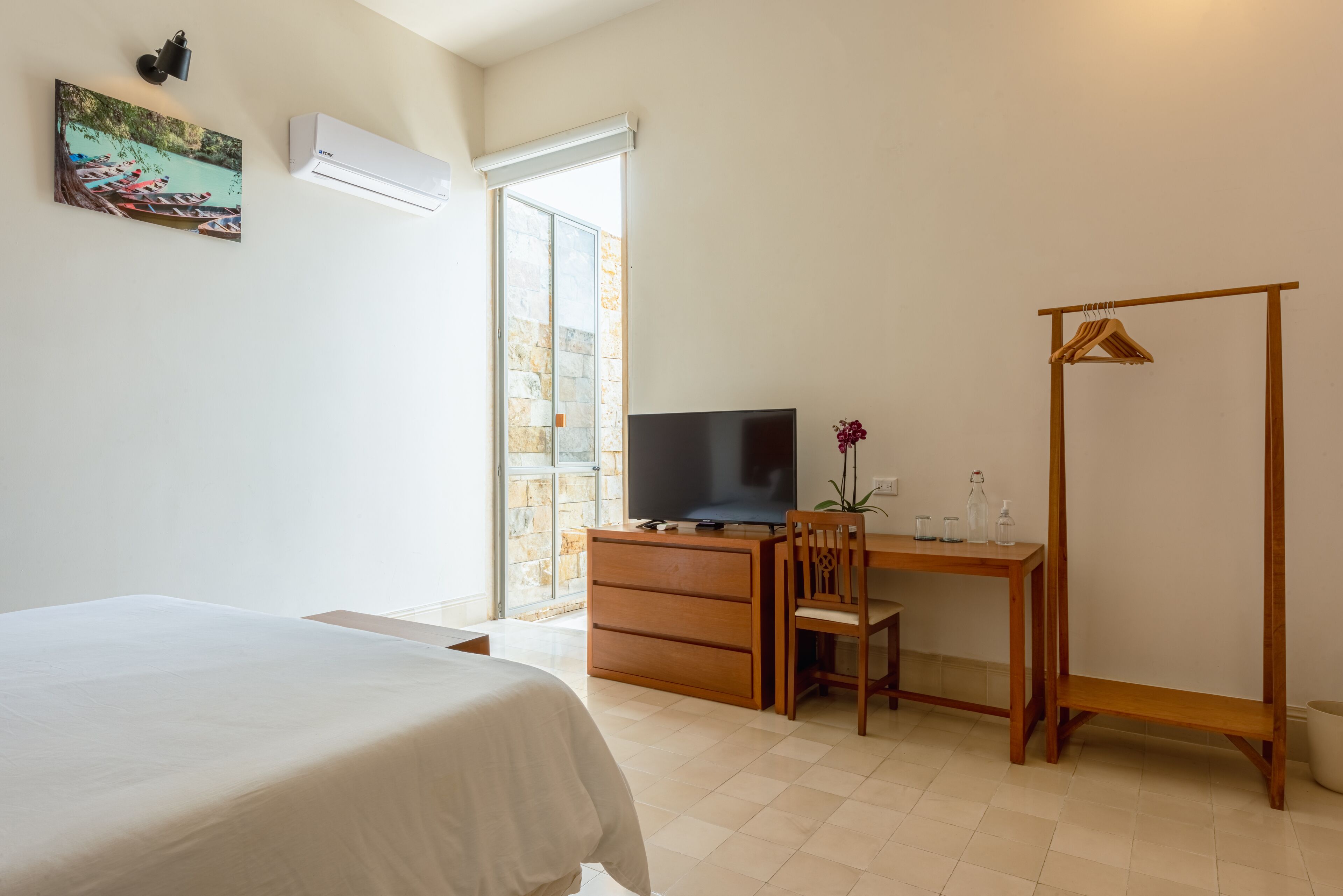 Un dormitorio con una cama, un escritorio con televisor, una silla de madera y un armario.