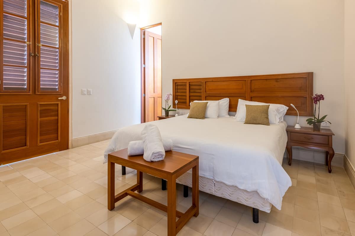 A neatly arranged bedroom with a large bed, bedside tables, and a small wooden table with towels.