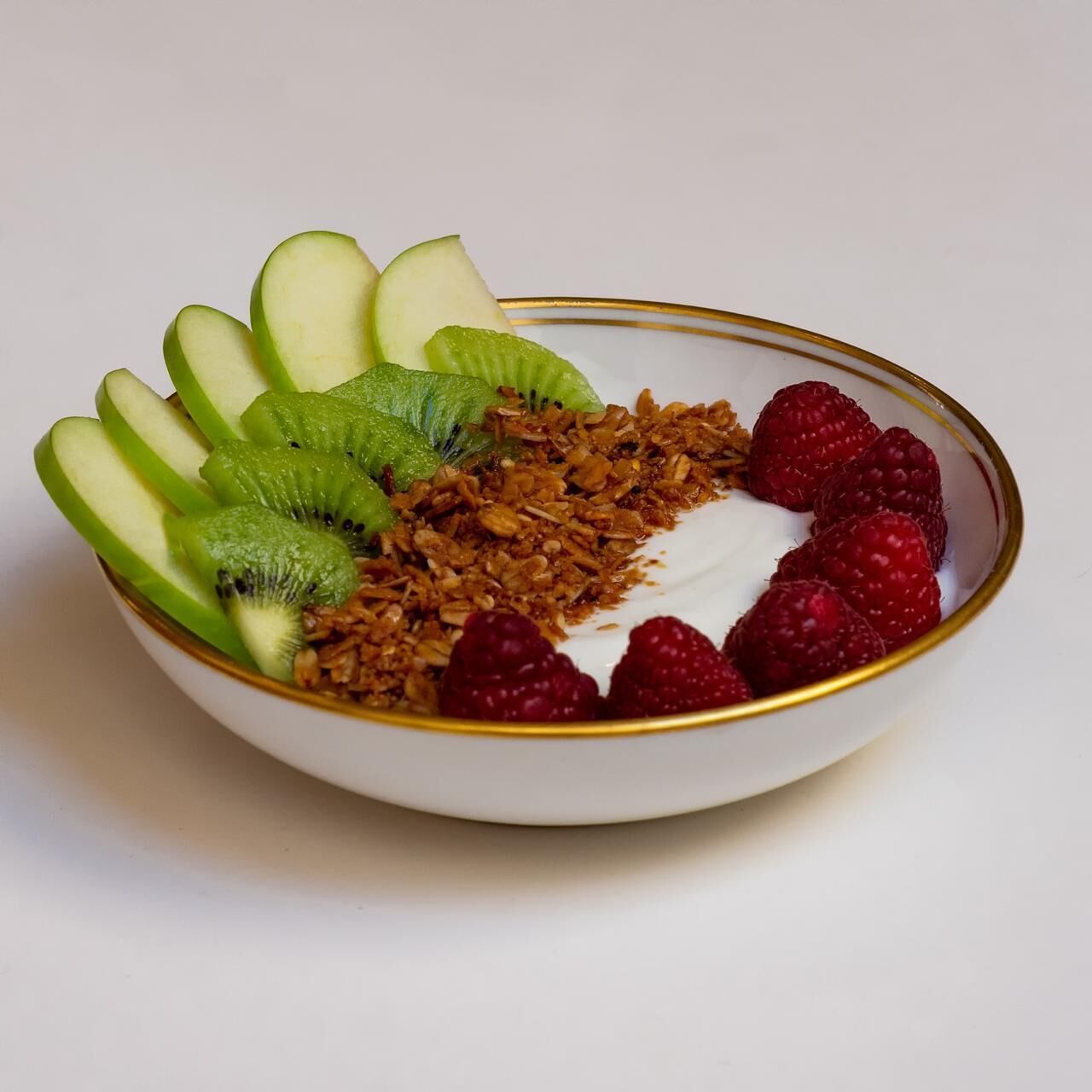 Un tazón con rodajas de manzana, kiwi, granola, frambuesas y yogur.