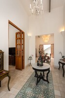 A spacious living area with a large wooden door, a chandelier, a dining table, and a patterned rug.
