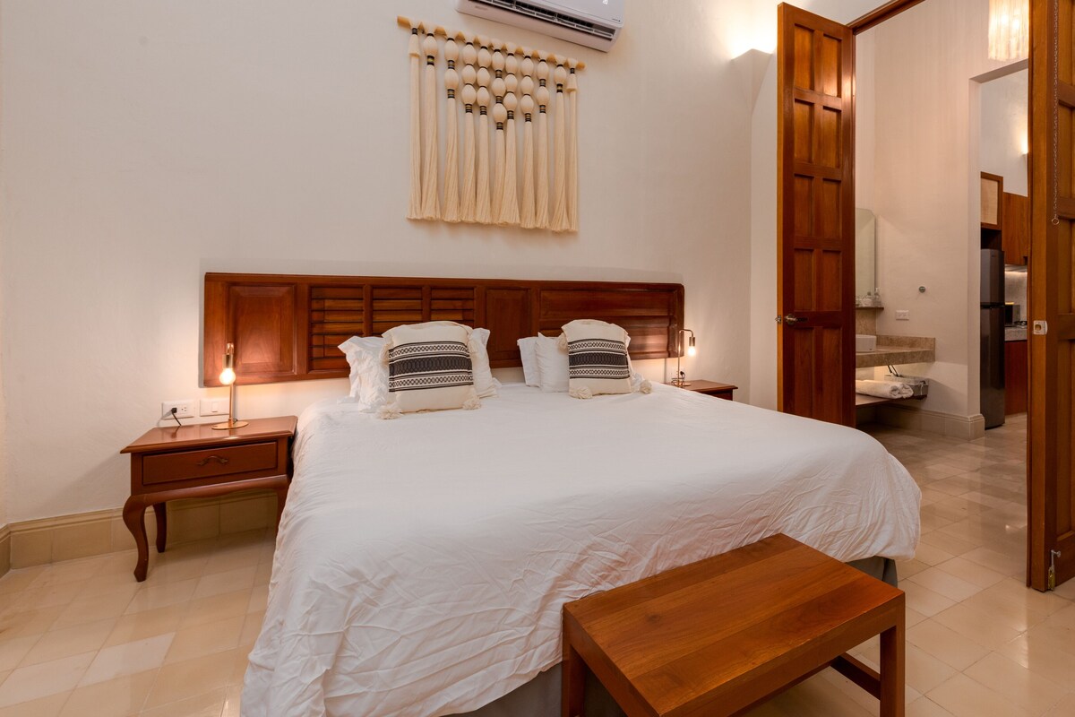 A neatly arranged bedroom with a wooden headboard, a bedside table with a lamp, and a bench.