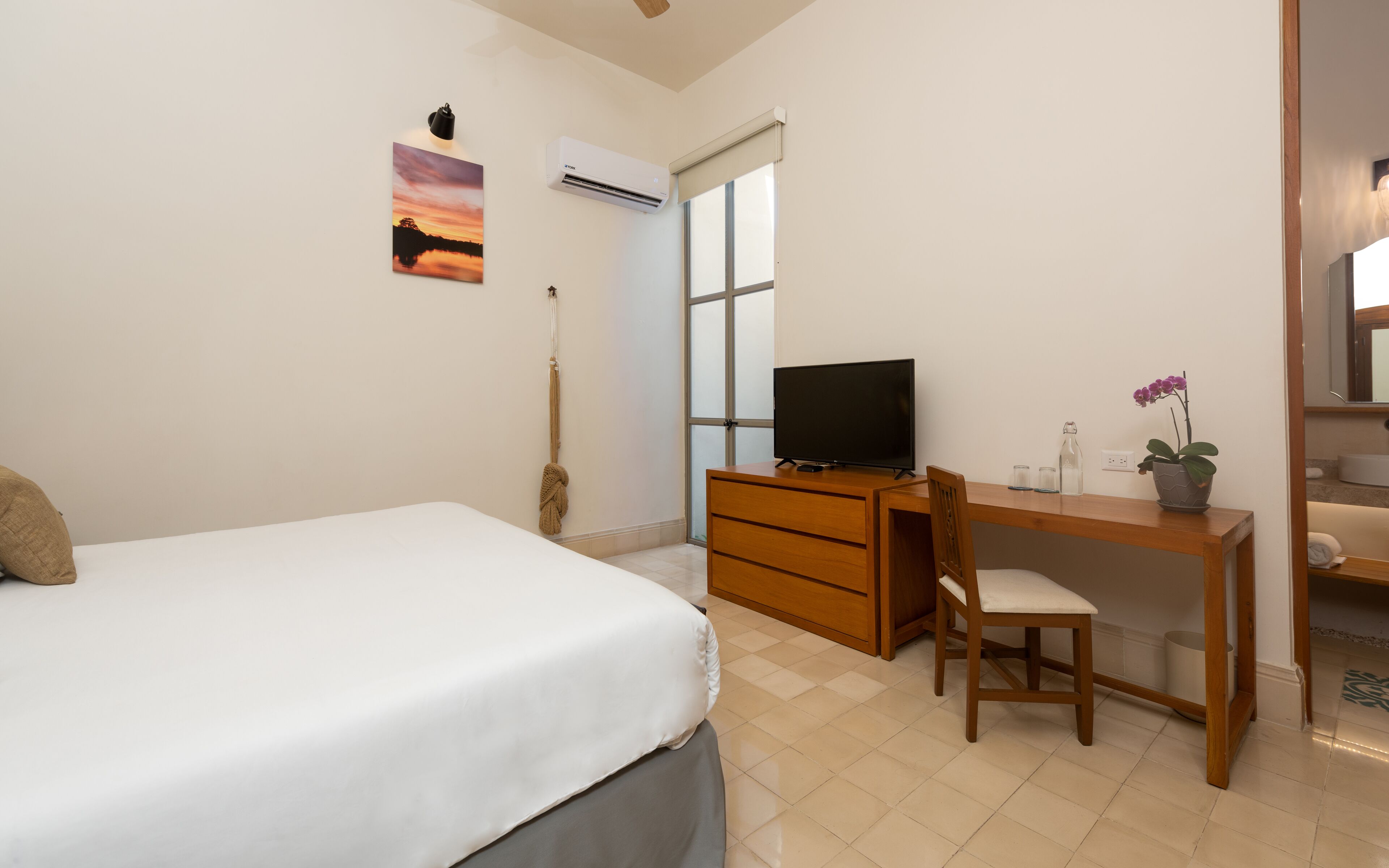 Un dormitorio con cama, escritorio, silla, televisor, aire acondicionado y ventana.