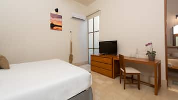 Un dormitorio con cama, escritorio, silla, televisor, aire acondicionado y ventana.