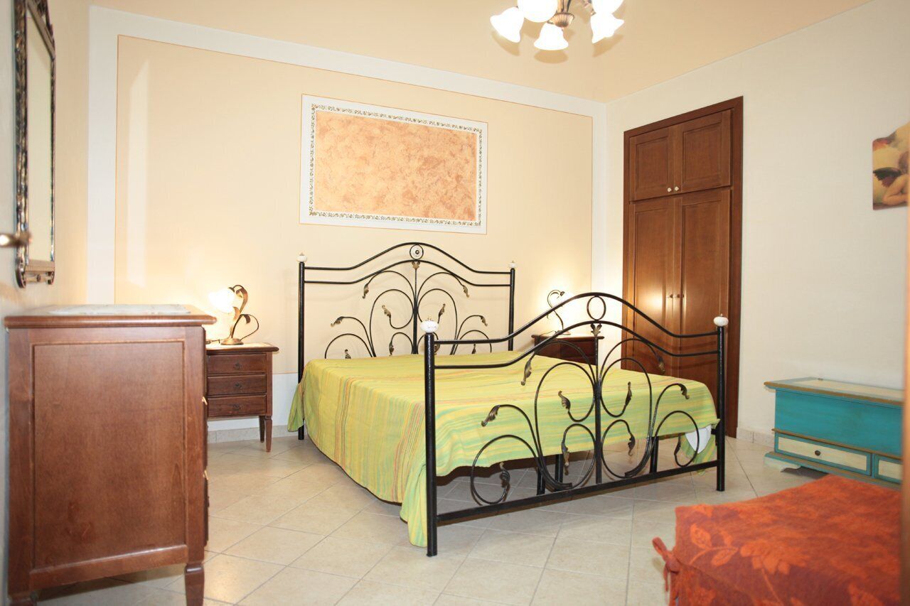A bedroom with a bed, a nightstand, a wooden wardrobe, and a dresser.