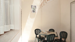 Uma pequena sala de jantar com uma mesa e quatro cadeiras, uma cortina estampada e um quadro pendurado na parede.