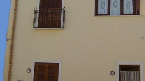 Um edifício de dois andares com fachada bege, persianas de madeira no andar térreo e uma varanda com grade de metal no andar superior.