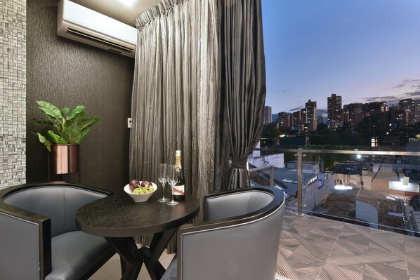 A modern dining area with a table set for two, a potted plant, and a view of the cityscape at dusk. - Luxury Combo Apartments with Jacuzzis and View (Medellín)