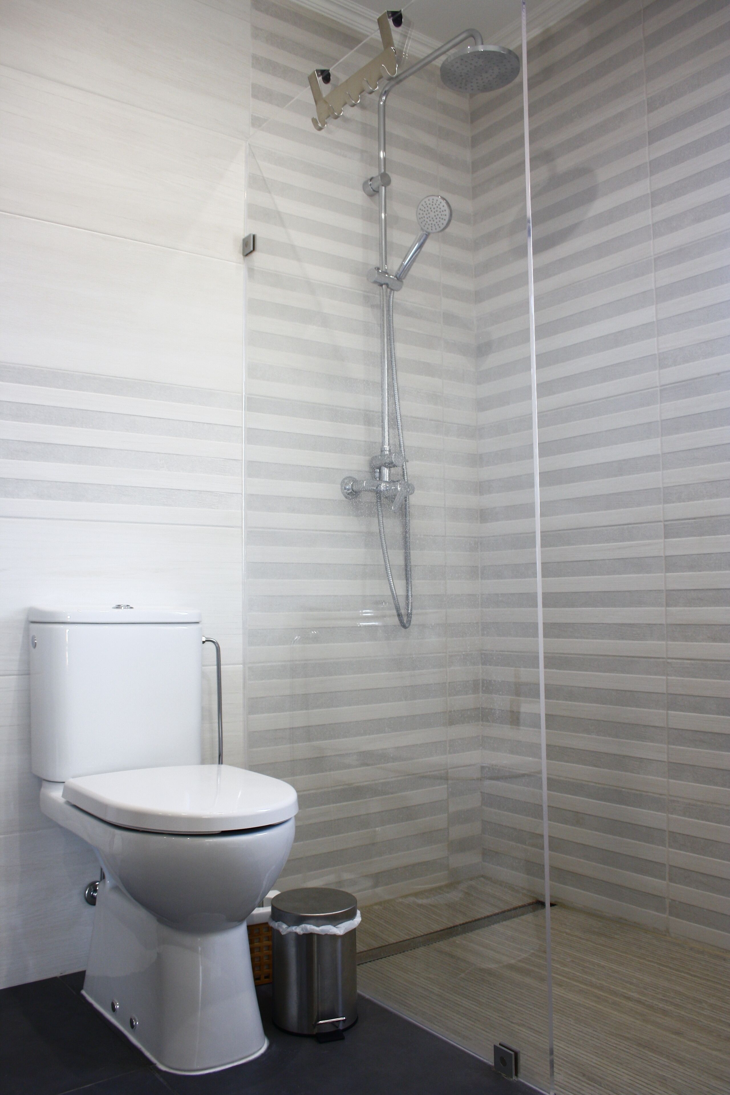 A modern bathroom with a toilet, a trash bin, and a glass-enclosed shower area.