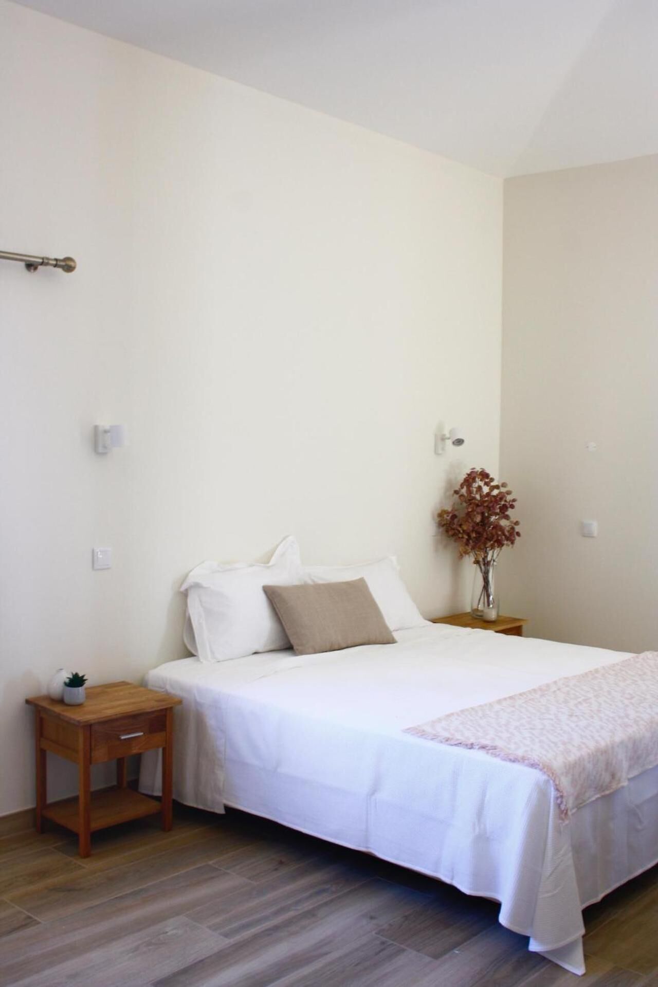A bedroom with a bed, a bedside table, a nightstand, and a vase with dried flowers.
