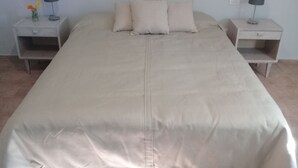 Ein ordentlich bezogenes Bett mit einer beigefarbenen Tagesdecke und Kissen, begleitet von zwei Nachttischen mit Lampen und einer Blumenvase.