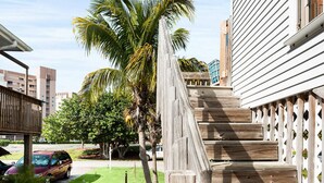 Una escalera de madera que lleva a una casa de fachada blanca, césped verde y una palmera.