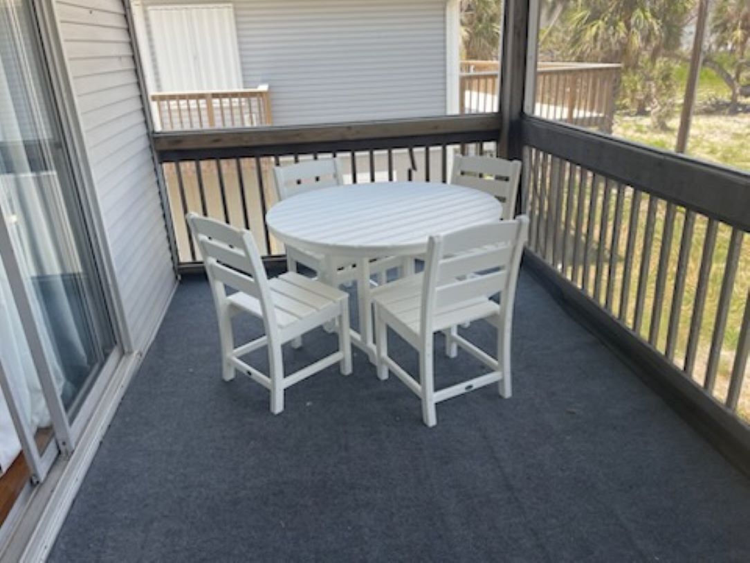 En overdækket terrasse med et rundt bord og fire hvide stole.