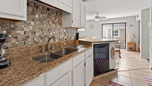 Una cocina con armarios blancos, encimera de granito, lavavajillas y salpicadero de mosaico.