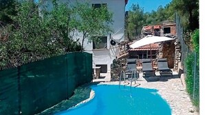 A swimming pool with a stone border, a white building with a red roof, and a stone wall in the background.