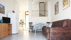 A compact living space with a sofa, a small table, a TV, and a refrigerator. - I tre Golfi Azzurra (San Vito Lo Capo)