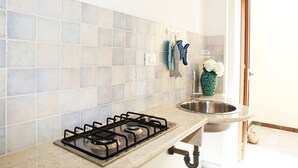 A kitchen with a gas stove, a sink, and a tiled backsplash. - I tre Golfi Azzurra (San Vito Lo Capo)