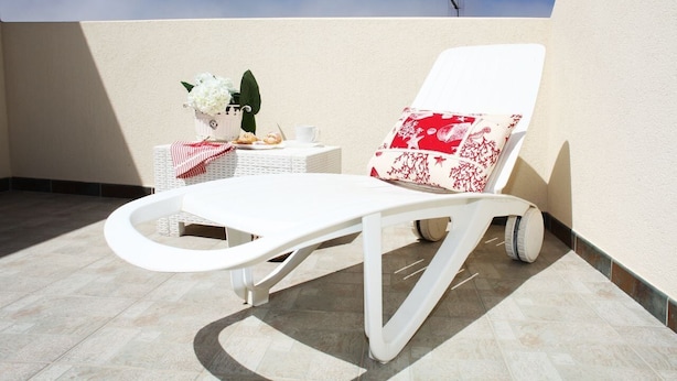A white lounge chair with a red and white patterned cushion, a small table with a white cup and a vase of white flowers, and a tiled floor. - I tre Golfi Azzurra (San Vito Lo Capo)