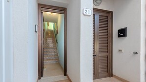 Un pasillo con una puerta de madera marcada '21', un buzón y una escalera que sube a un piso superior.