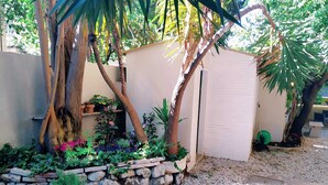 Un jardín con un muro de piedra, un cobertizo pequeño y diversas plantas.