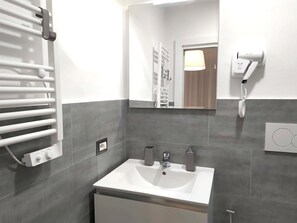 A modern bathroom with a white sink, a mirror, a towel rack, and a hairdryer mounted on the wall. - Garden House - Luxury Guest House (Rome)