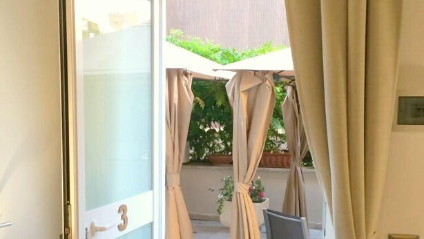 Puerta abierta que da a un balcón con vistas a un jardín y una silla.