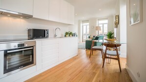 A modern kitchen with white cabinets, a Bosch oven, and a microwave. There is a dining area with a glass table and wooden chairs.